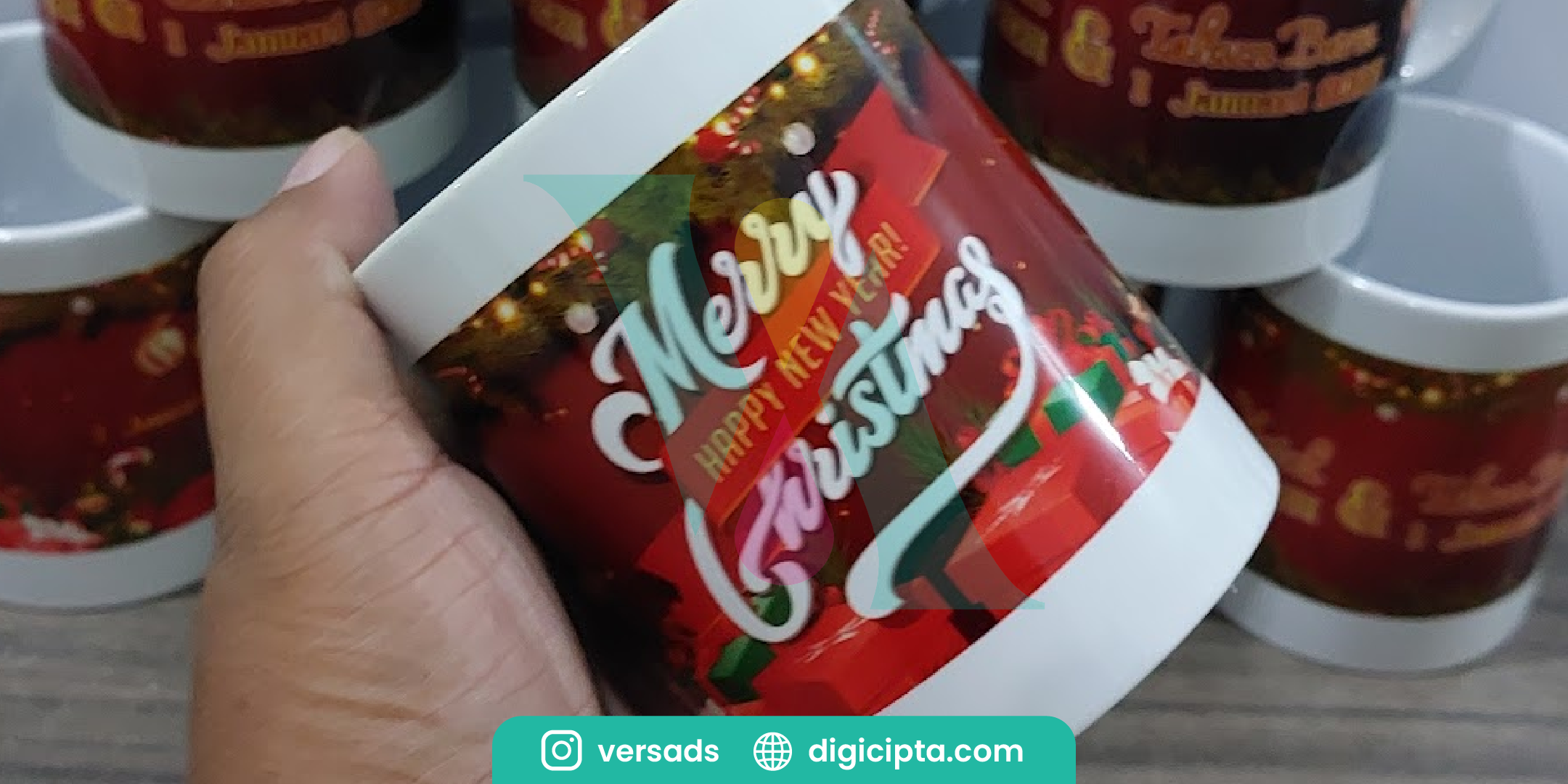 Tangan memegang mug putih dengan desain merah bertuliskan “Merry Christmas” dan “Happy New Year”, dihiasi gambar kado dan ornamen Natal, menciptakan suasana hangat dan meriah khas perayaan akhir tahun.